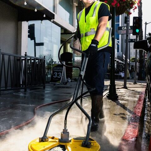 Worker operating a powered surface cleaner outdoors