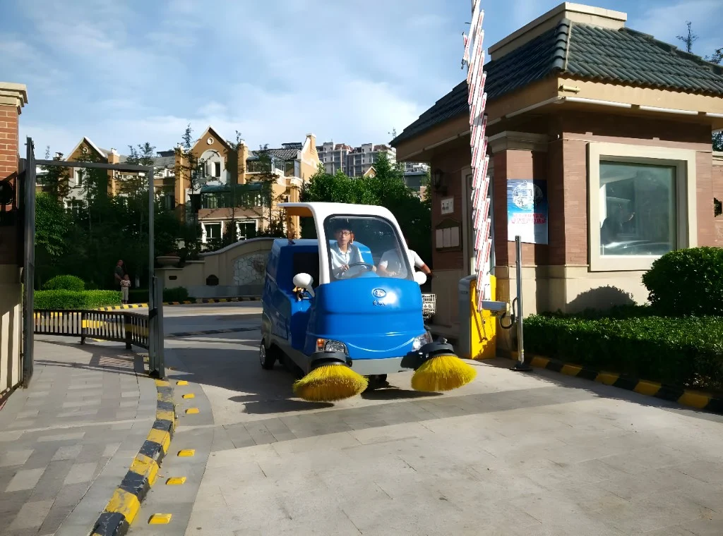 Operator driving a compact electric sweeper through a site entrance